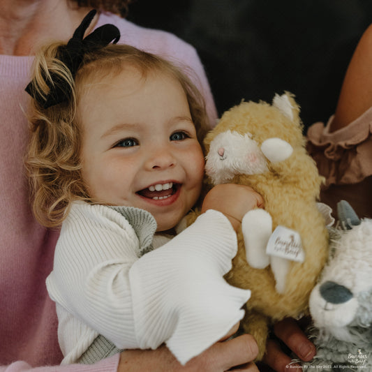 Little toddler girl smiling and holding in her hands the Wee Alley Cat Plush toy in yellow - Bunnies By The Bay