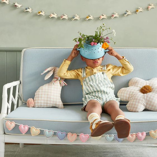 Little boy sitting on a blue couch with a bunny pillow and flower pillow in pink gingham