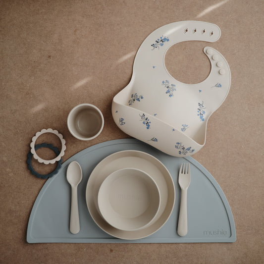 Mushie Silicone Bib in Lilac with dinnerware and placemat in blue