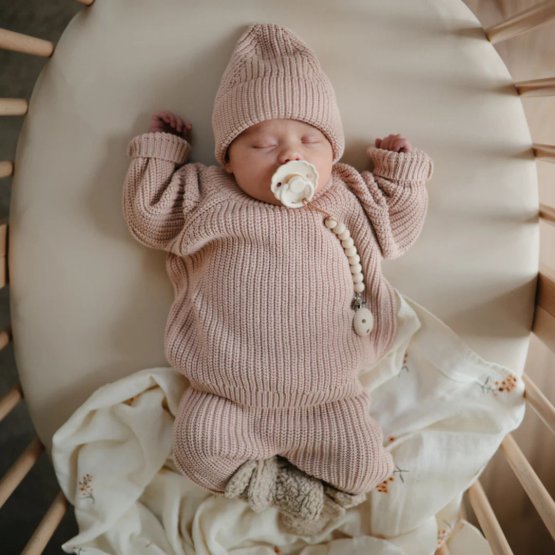 Baby girl sleeping in her crib and wearing a pink beanie, pink sweater and pink pants. 